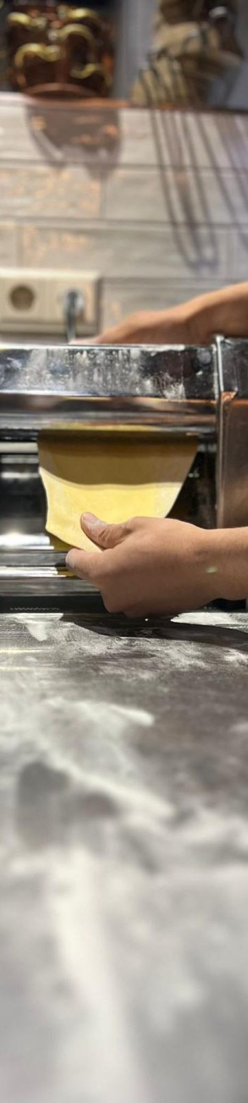 Een hand rolt vers deeg uit met een pastamaker op een werkblad.